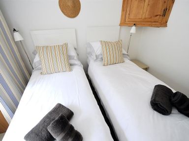 A bedroom with two single beds each with white bedding striped pillows towels on the foot of the beds bedside lamps and a wooden wall cabinet at 10 Cobb Terrace in Lyme Regis