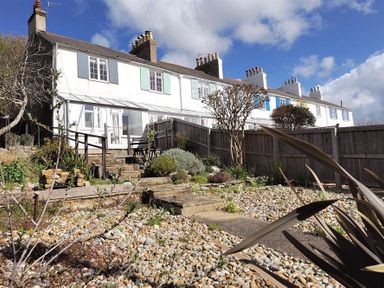 A row of white terraced houses with colored shutters and a garden with stone steps and gravel at 10 Cobb Terrace Lyme Regis