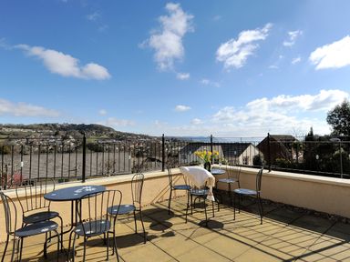 An outdoor terrace with black metal tables and chairs overlooking houses and hills at Jurassic Sea View in Lyme Regis