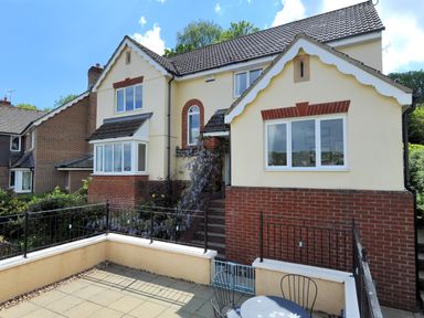 An outdoor patio with chairs and a table in front of a two story house with cream and brick exterior Jurassic Sea View Lyme Regis