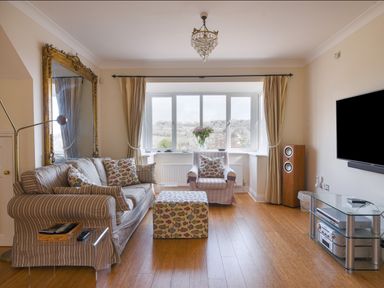 A living room with a sofa armchair ottoman large mirror flat screen tv speakers and window with curtains at Jurassic Sea View Lyme Regis