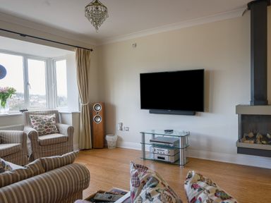 A living room with armchairs a wall mounted tv and a fireplace at Jurassic Sea View in Lyme Regis