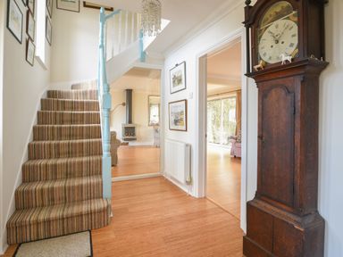 A hallway with a staircase and grandfather clock with views into adjacent rooms at Jurassic Sea View in Lyme Regis