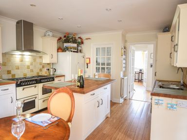 A kitchen with a wooden table and chairs a central island with bottles and glasses a stove refrigerator and a sink at Jurassic Sea View Lyme Regis