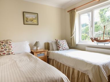 A bedroom with two single beds a nightstand with a lamp a framed picture on the wall and a window with a wooden boat model at Jurassic Sea View in Lyme Regis