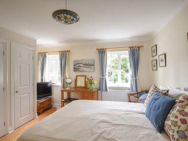 A bedroom with a bed a desk a TV and two windows with blue curtains at Jurassic Sea View in Lyme Regis