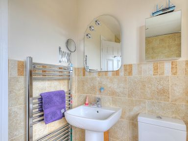 A bathroom with a sink toilet heated towel rail with a purple towel and two mirrors at Jurassic Sea View in Lyme Regis