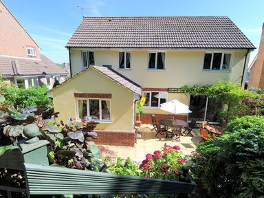 A backyard patio with outdoor table chairs and umbrella next to a two story yellow house with multiple windows at Jurassic Sea View Lyme Regis