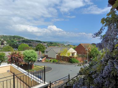 A neighborhood street with houses trees and flowers with a view of hills and the sea at Jurassic Sea View in Lyme Regis