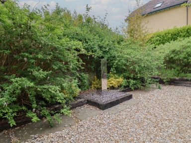 A garden with a metal sculpture surrounded by bushes and gravel at Yard Cottage in Rousdon