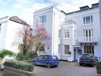 A white multi-story building with parked cars and blossoming trees in front at The Penthouse in Lyme Regis