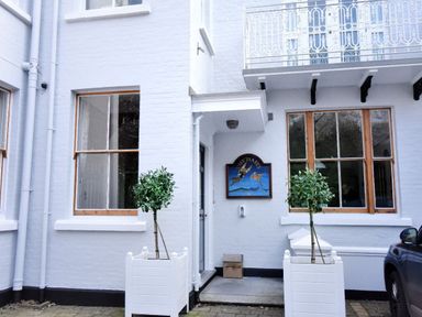 An exterior view of a white brick building with two windows a door two potted plants and a car at The Penthouse in Lyme Regis