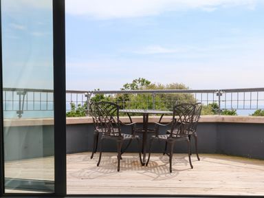 A balcony with a metal table and four metal chairs overlooking trees and water at The Penthouse in Lyme Regis