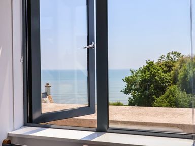 A window open showing a view of the sea trees and a rooftop at The Penthouse in Lyme Regis