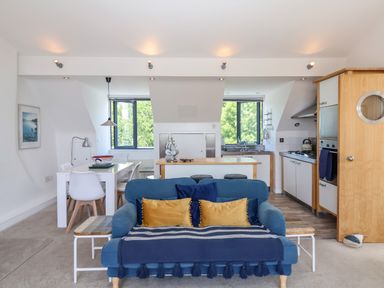 A living room with a blue sofa a dining table and an open kitchen at The Penthouse in Lyme Regis