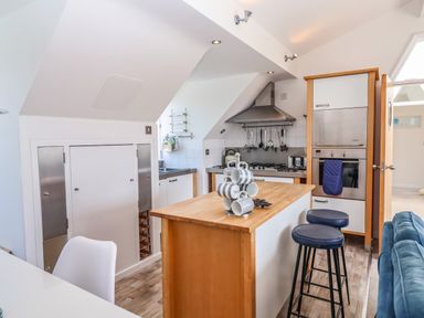 A kitchen with an island and stools next to a blue sofa at The Penthouse in Lyme Regis
