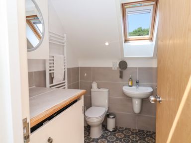 A bathroom with a toilet, sink, round mirror, window, towel rack, and patterned floor at The Penthouse in Lyme Regis