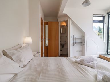 A bedroom with a bed with white linens two wooden doors a lamp and a window at The Penthouse in Lyme Regis