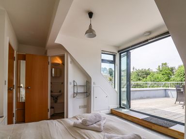 A bedroom with an open door to a bathroom and glass doors opening to a terrace at The Penthouse in Lyme Regis