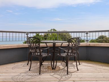 A balcony with a metal table and four chairs overlooking trees and the sea at The Penthouse in Lyme Regis