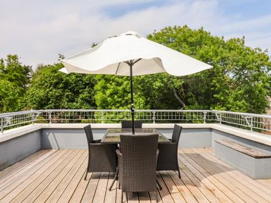 An outdoor deck with a table, chairs, and a large umbrella surrounded by trees at The Penthouse in Lyme Regis