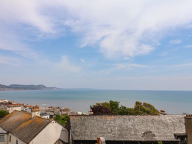 A view of rooftops trees and the sea with hills in the distance at The Penthouse in Lyme Regis