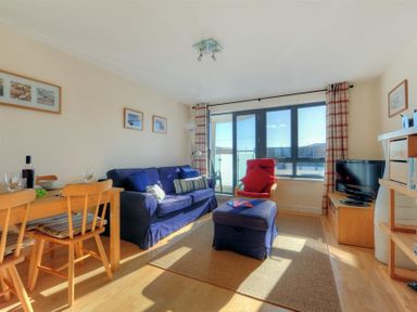 A living room with a blue sofa red chair wooden dining table and a television at 8 Driftwood in West Bay