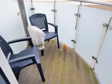 A balcony with two black plastic chairs one with a white throw and a bottle and glass on the wooden floor at 8 Driftwood in West Bay
