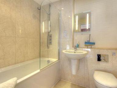 A bathroom with a bathtub shower combination pedestal sink toilet and a small blue boat decoration on the ledge at 8 Driftwood in West Bay