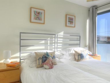 A bedroom with two single beds side by side with metal headboards two bedside tables with lamps books and cushions with house designs at 8 Driftwood in West Bay