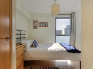 A bedroom with a bed white bedding a wooden chest of drawers and a window with curtains at 8 Driftwood in West Bay