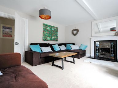 A living room with a brown sectional sofa and blue pillows a wooden coffee table a fireplace with a mirror above it and wall art at Mermaid House in Lyme Regis