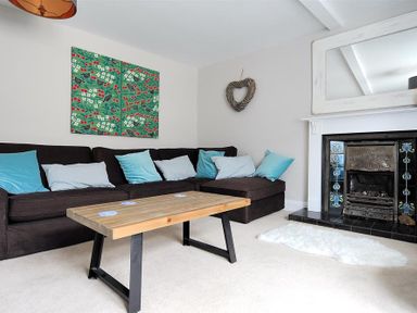A living room with a dark sofa with blue and white cushions a wooden coffee table a fireplace with decorative tiles and a mirror above it and a heart shaped wall decoration at Mermaid House in Lyme Regis