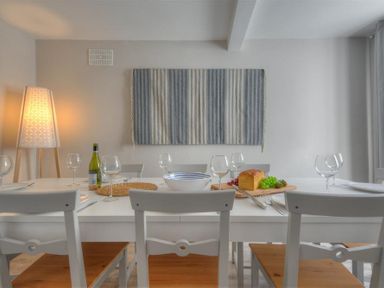 A dining room with a white table set with wine glasses a loaf of bread grapes a bottle of wine and a lamp at Mermaid House in Lyme Regis