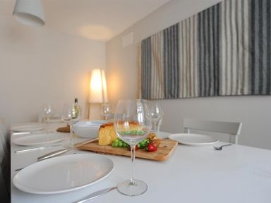 A dining table set with white plates wine glasses and bread with grapes and strawberries on a cutting board in a room at Mermaid House in Lyme Regis
