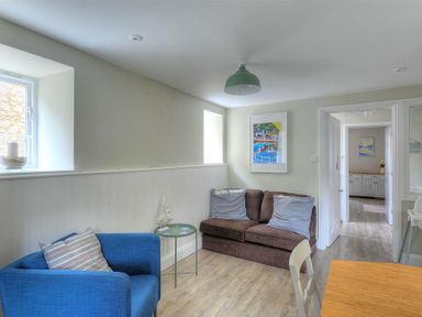 A sitting room with a blue armchair and brown sofa with cushions and a side table with a model sailboat at Mermaid House in Lyme Regis