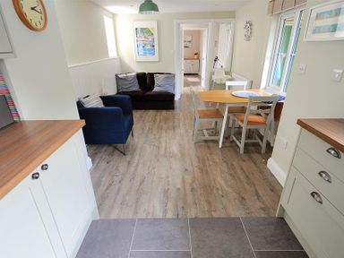 A dining area with a table and four chairs next to a living space with two sofas and cushions at Mermaid House Lyme Regis