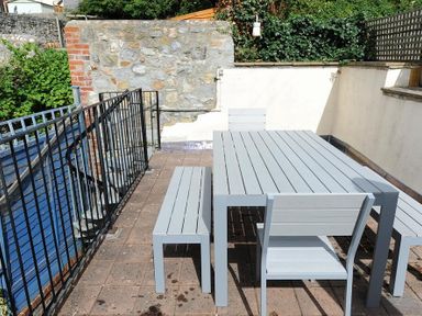 An outdoor patio area with a grey table and matching chairs and benches surrounded by stone and brick walls