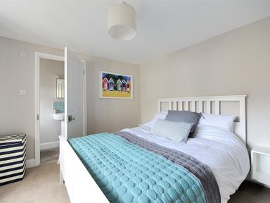 A bedroom with a white bed with blue and gray bedding a striped laundry basket and a colorful painting at Mermaid House in Lyme Regis