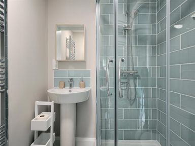 A bathroom with a pedestal sink a mirror a shower with blue tiled walls and a white storage rack at Mermaid House Lyme Regis