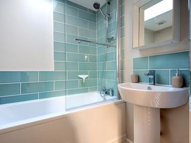 A bathroom with a bathtub shower combination blue tiled walls and a sink with a mirror at Mermaid House Lyme Regis