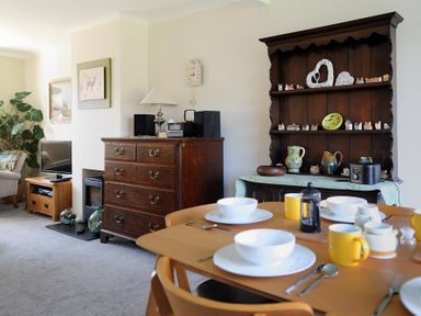 A dining area with table set for four and wooden shelves with ceramics in a living room at Woody View in Colyton