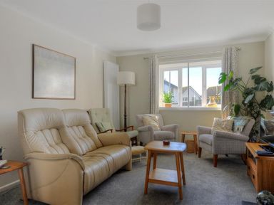 A living room with a beige leather sofa two grey armchairs a green chair wooden tables and a television at Woody View in Colyton