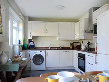 A kitchen with white cabinets a washing machine an oven a refrigerator and a wooden table at Woody View in Colyton