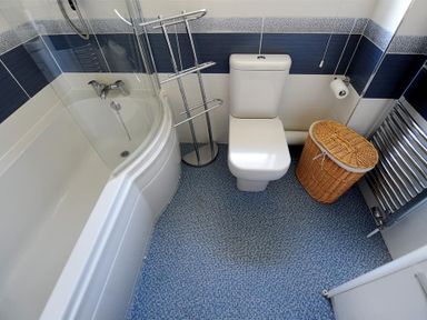 A bathroom with a bathtub shower combo a toilet a wicker laundry basket and a towel radiator at Woody View in Colyton