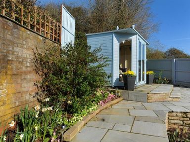 A garden with a small shed a flower bed and stone paving at Woody View in Colyton