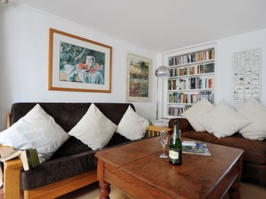 A living room with brown sofas white cushions a wooden table a bookshelf and paintings at 24 Mill Green Lyme Regis