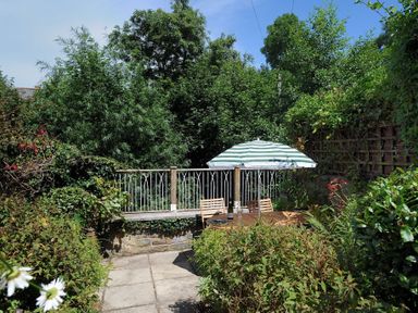 A garden patio with a table chairs and a striped umbrella surrounded by plants at 24 Mill Green Lyme Regis