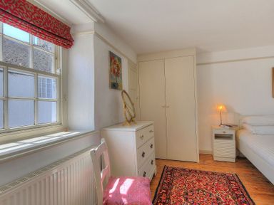 A bedroom with a window a dresser a chair a rug a wardrobe a bedside table with a lamp and a bed at 24 Mill Green in Lyme Regis