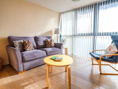 A living room with a purple sofa and patterned cushions a round wooden coffee table and a blue armchair with a cushion at 2 Driftwood in West Bay